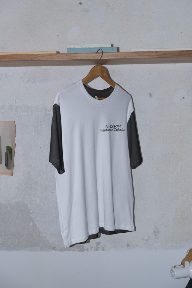 White and black raglan t-shirt mockup hanging on wooden hanger against concrete wall, with text detail, for fashion design presentation.